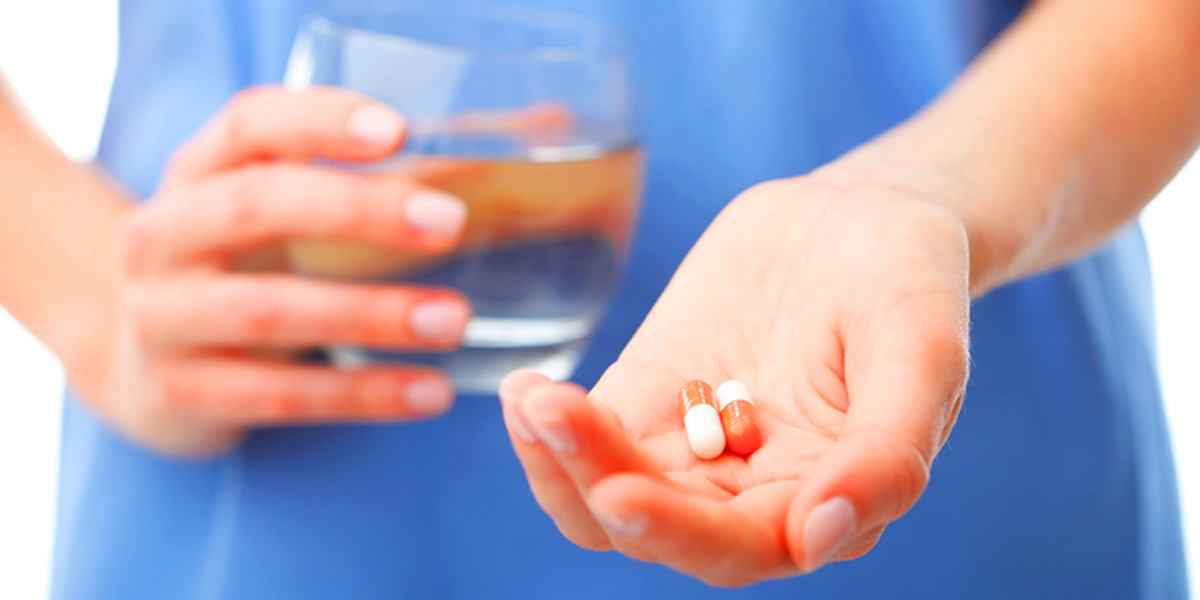 patient holding glass of water and medicine capsules